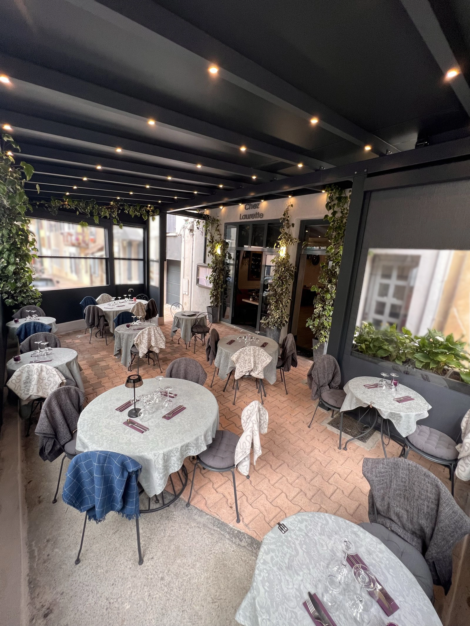 Terrasse couverte du restaurant Chez Laurette avec tables dressées, plantes vertes et guirlandes lumineuses